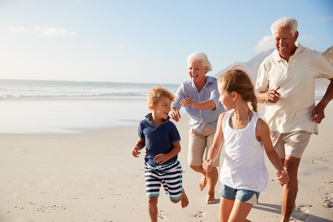 Afbeelding van een oudere man en vrouw die op het strand, al lachend achter 2 jonge kinderen lopen
